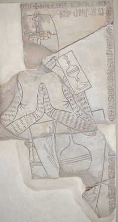 Gravstøtte fra andre halvdel av 1200-tallet funnet i Nidarosdomen. Den uidentifiserte ridderen har brynje og tønnehjelm. Skjoldmerket (våpenskjoldet hans) viser en pokal og en palmegren som peker mot at han har vært på pilegrimsreise eller korstog. Minjatyrskoldene på skuldrene (kun et ses her) er for ekstra beskyttelse, samtidig som det viser ridderens identitet. Foto: Ola Onsrud 2010